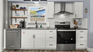 Una cocina moderna con armarios blancos, una estufa de acero inoxidable y una ventana con vistas a una terraza de madera.