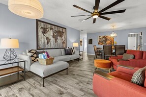 A modern living room with a sofa, ottoman, and a red couch. There is a dining area with a table and chairs. - Cozy & Spacious 2-bedroom suite in gorgeous Orlando ~ 6 guests & close to it all (Orlando)