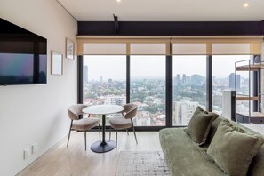 Ein modernes Wohnzimmer mit Blick auf die Stadt, einem runden Tisch mit Stühlen und einem grünen Sofa.