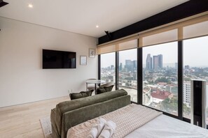 Ein modernes Schlafzimmer mit Blick auf die Stadt, einem Flachbildfernseher, einem Sofa und einem kleinen Tisch.