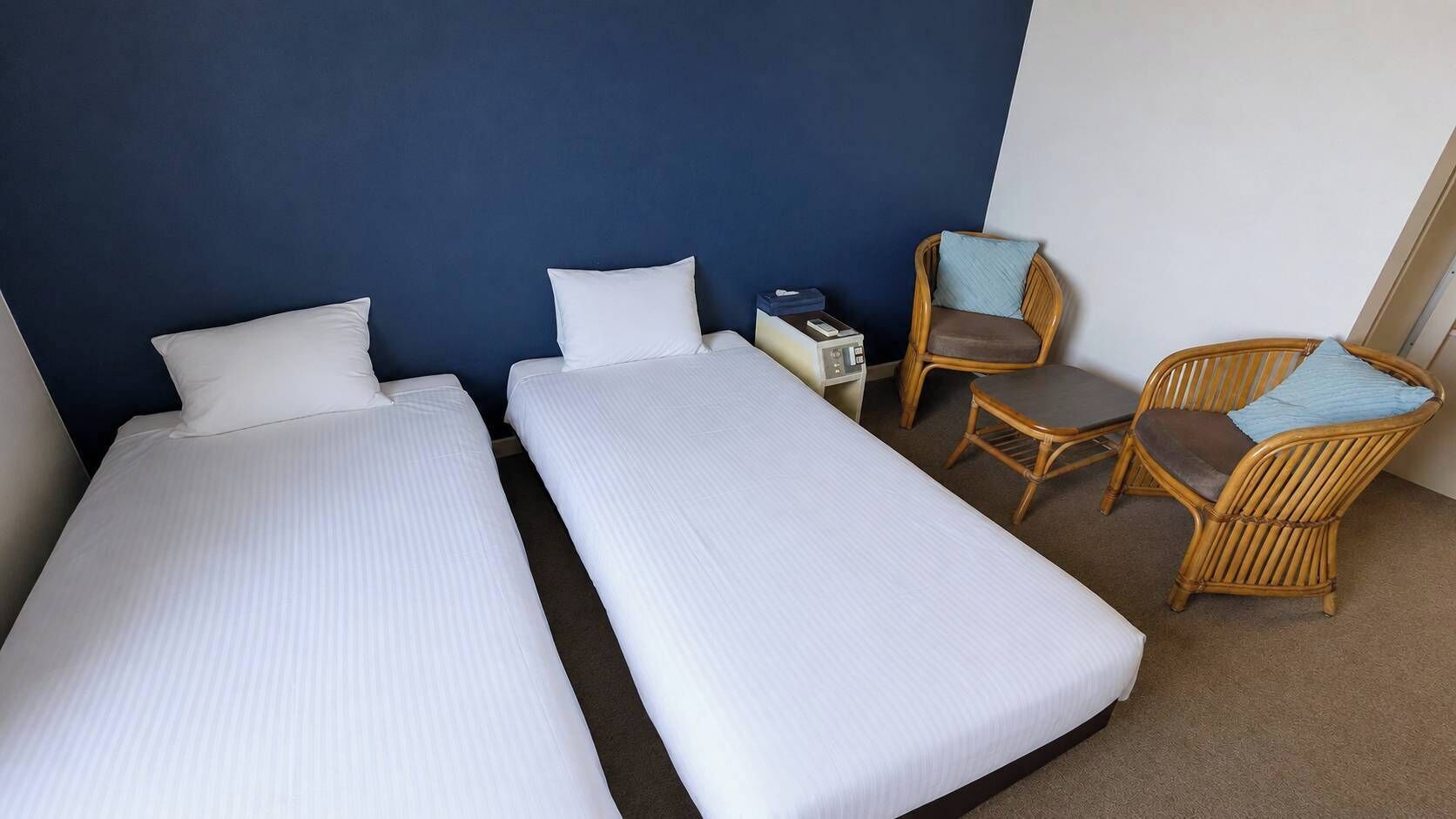 Et hotelværelse med to enkeltsenge, et lille skrivebord med telefon og to fletstole.