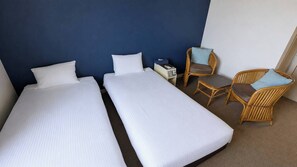 Una habitación de hotel con dos camas individuales, un escritorio pequeño con teléfono y dos sillas de mimbre.