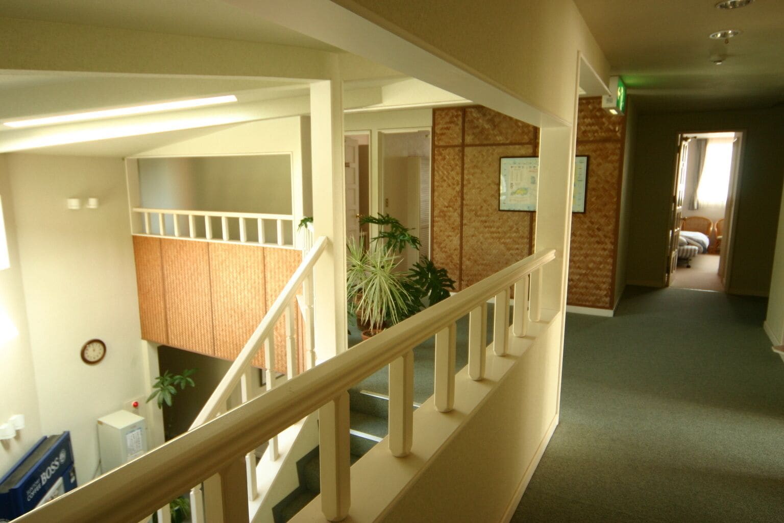 A hotel corridor with a staircase, a clock, and a plant.