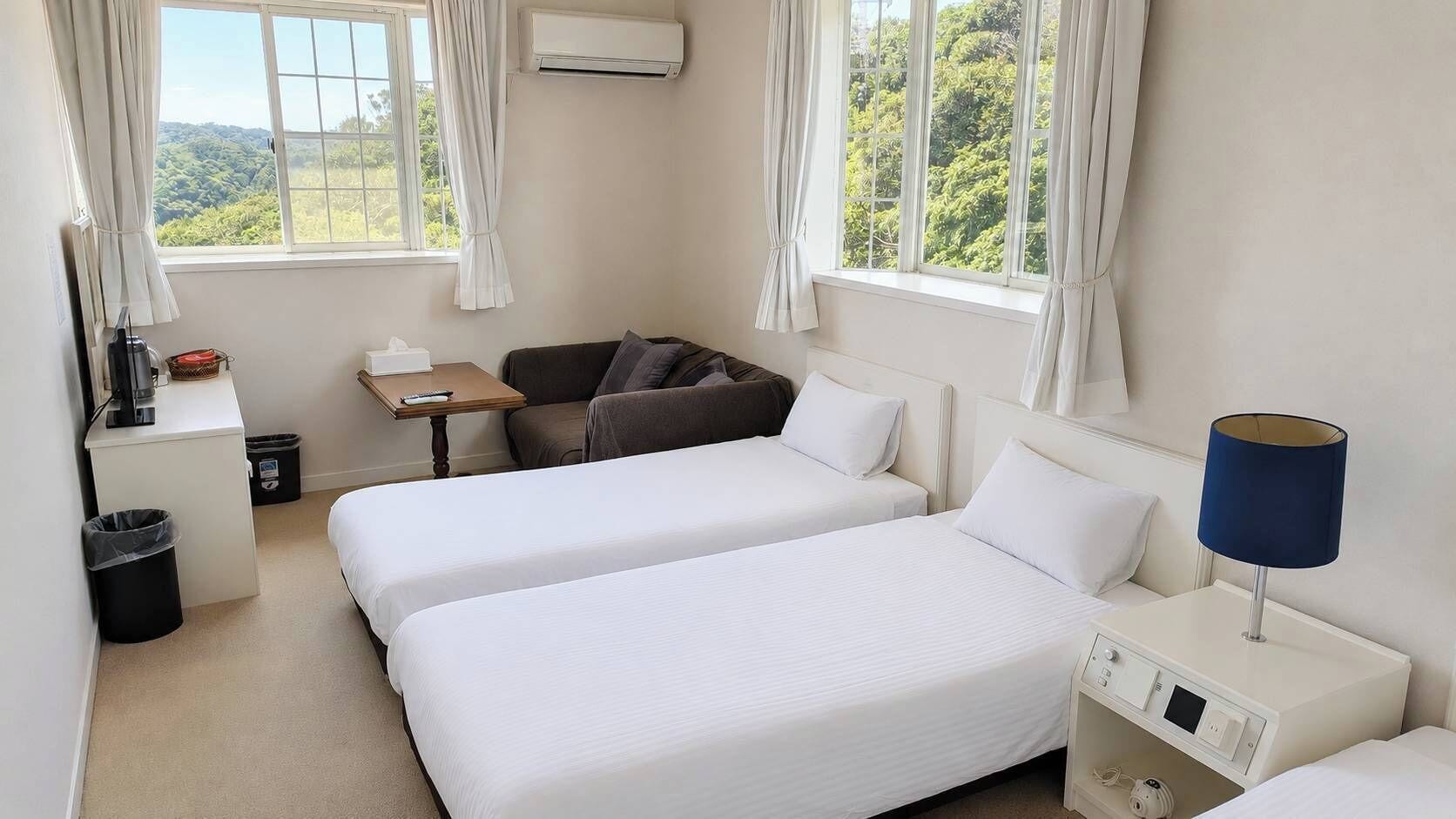 Habitación de hotel con dos camas, un escritorio, una silla, una lámpara y vistas a zonas verdes.