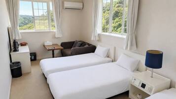A hotel room with two beds, a desk, a chair, a lamp, and a view of greenery.