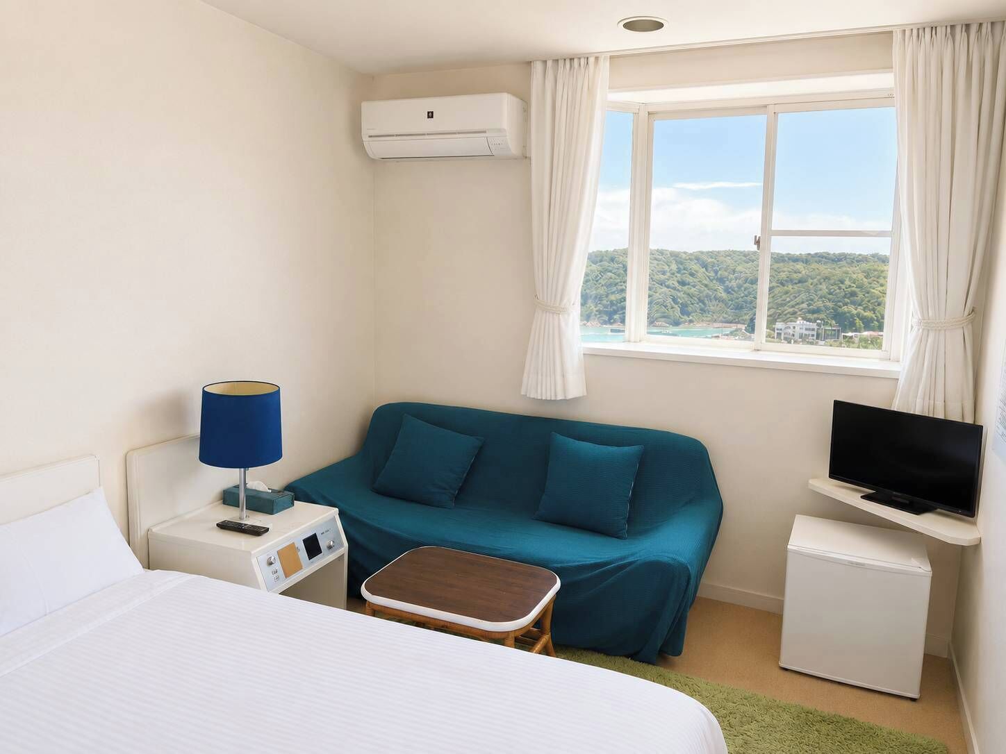 A hotel room with a bed, a sofa, a small table, a TV, and a window with a view of a green landscape.