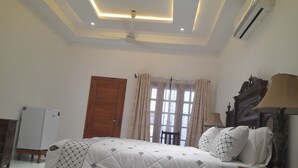 Ein Schlafzimmer mit einem Bett, Deckenventilator, Holztür, einem Fenster mit Vorhängen und einer Nachttischlampe.
