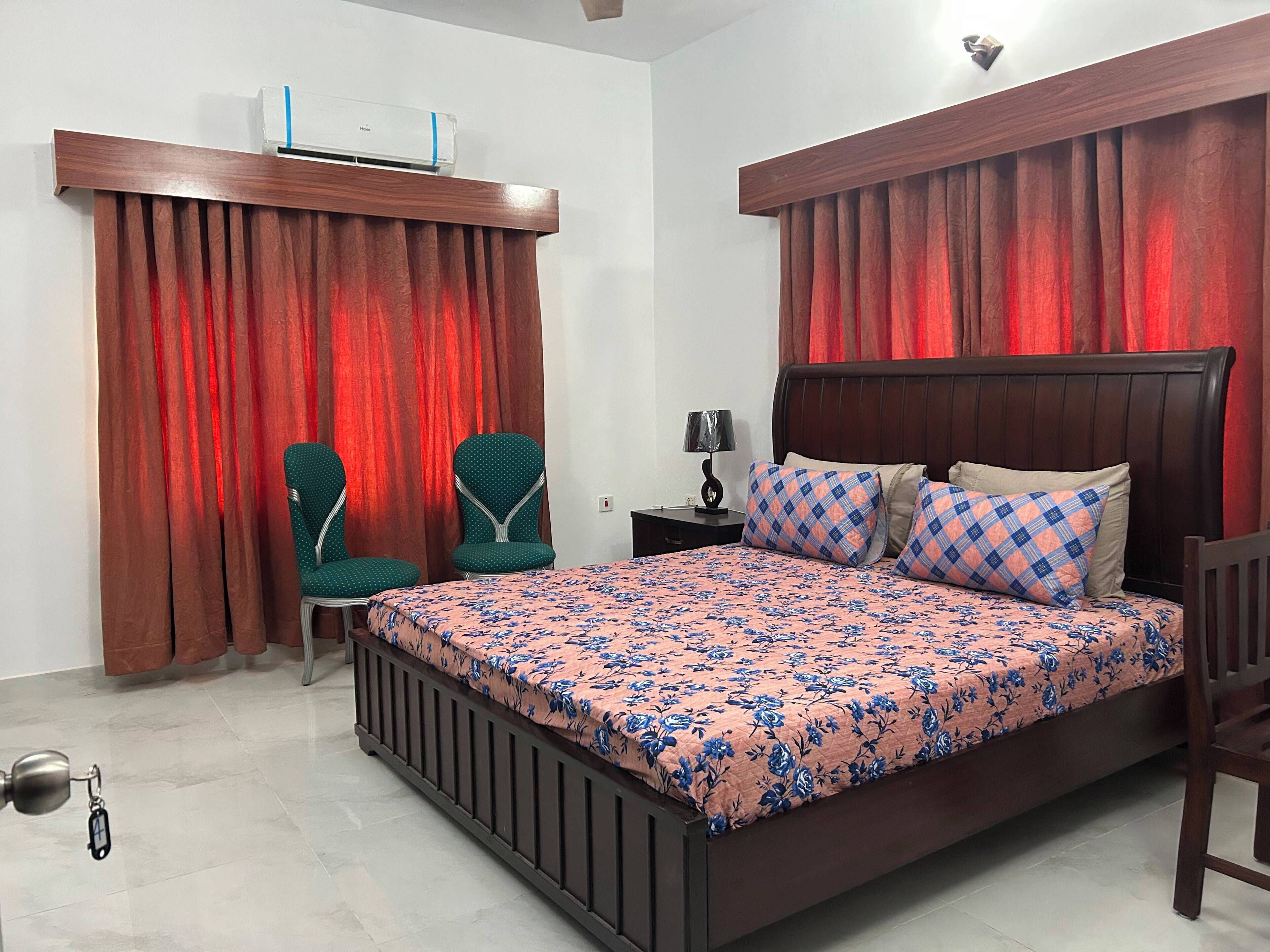 Une chambre à coucher avec un lit, deux chaises, une table de chevet, une lampe et un ventilateur de plafond.