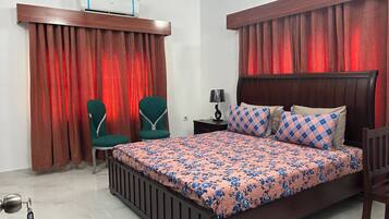 Une chambre à coucher avec un lit, deux chaises, une table de chevet, une lampe et un ventilateur de plafond.