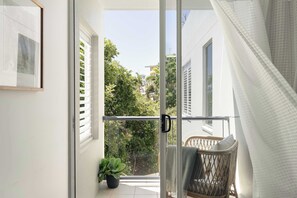 Ein Balkon mit einem Korbstuhl, einem Blumentopf und Blick auf Grünflächen und Gebäude.