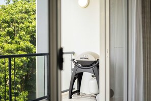 Un balcon avec un barbecue, une bouteille de gaz blanche et un appareil fixé au mur.