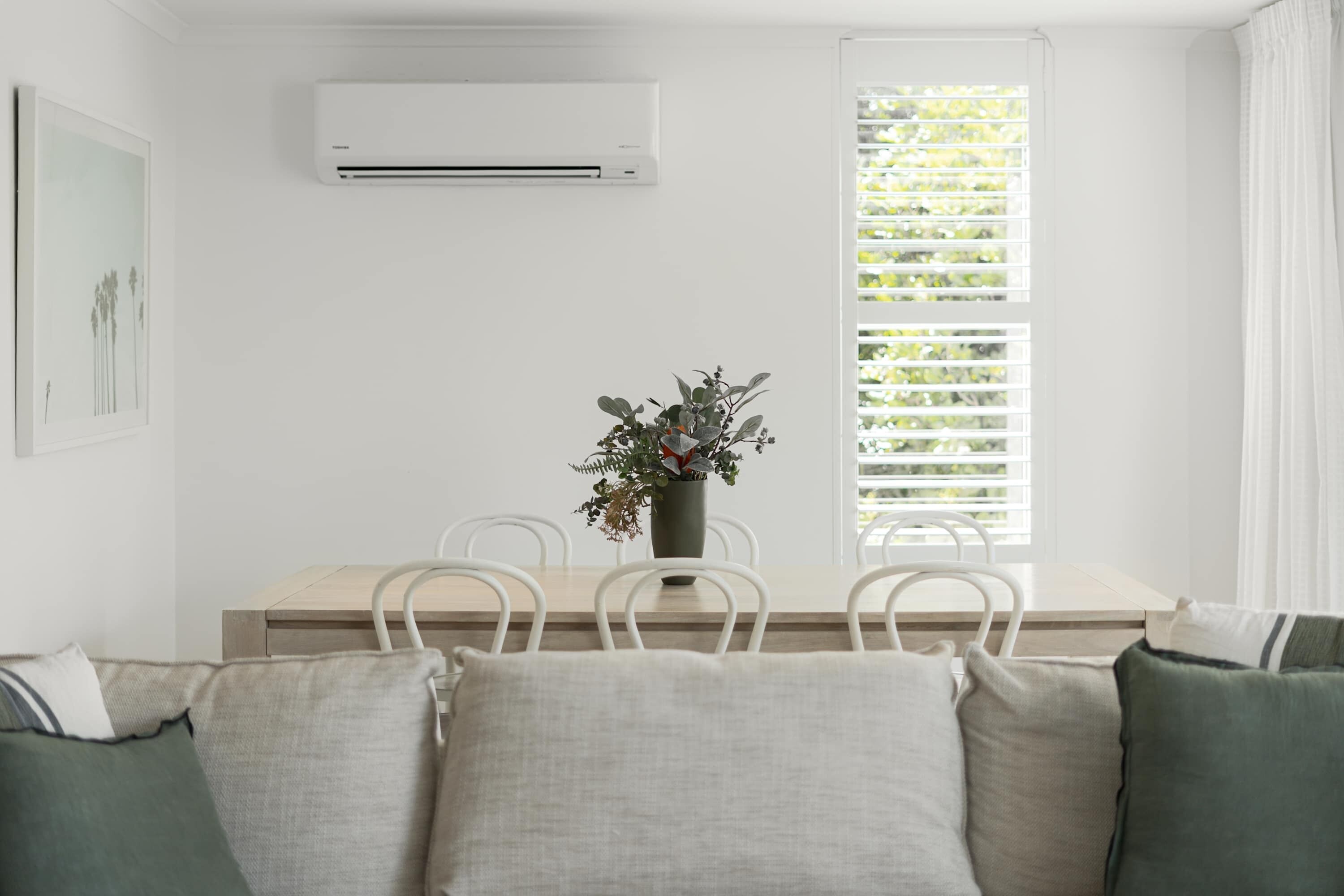 Una habitación con una mesa de comedor, sillas, una planta en maceta, un equipo de aire acondicionado y una ventana con persianas.