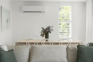 Ein Zimmer mit Esstisch, Stühlen, einer Zimmerpflanze, einer Klimaanlage und einem Fenster mit Jalousien.