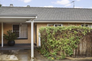 Ein Wohnhaus mit Ziegeldach, einer überdachten Veranda, einem Blumentopf und einer dichten Hecke.