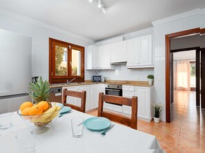 Eine moderne Küche mit weißen Schränken, einem Fenster mit Holzrahmen, einer Mikrowelle und einem Essbereich mit Tisch für zwei Personen.