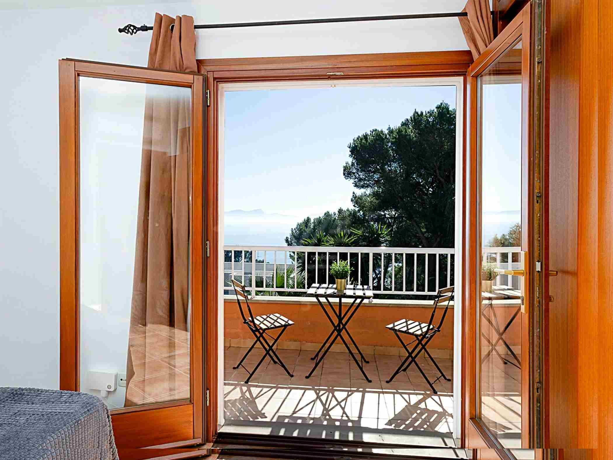 Ein Zimmer mit einer Schiebetür und einem Ausgang auf einen Außenbalkon mit Tisch und Stühlen.