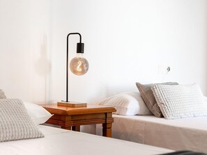 Ein Schlafzimmer mit Nachttisch aus Holz, einer Tischlampe, einem Bett mit Kissen und einer Steckdose.