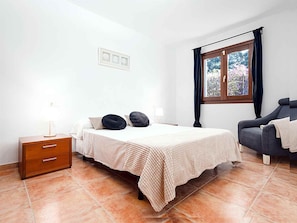 A bedroom with a bed, a nightstand, a chair, a window with curtains, and a wall-mounted light switch. - 'Chalet Mirador', with panoramic views of the Mediterranean Sea (Alcudia)
