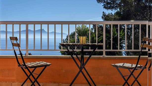 Ein Balkon mit zwei Stühlen und einem Tisch, der einen schönen Blick auf Meer und Berge bietet.