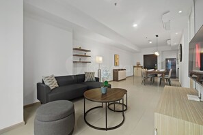 Ein modernes Wohnzimmer mit einer Couch, Hocker, Couchtisch und einem Essbereich mit Stühlen und Tisch.