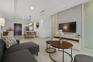 A modern living room with a sofa, a coffee table, a TV, and a dining area with chairs and a table. - Kavri by Kozystay - Kuningan (South Jakarta)
