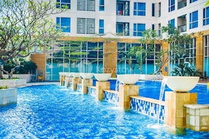A swimming pool with multiple water features and a modern building in the background. - Kavri by Kozystay - Kuningan (South Jakarta)