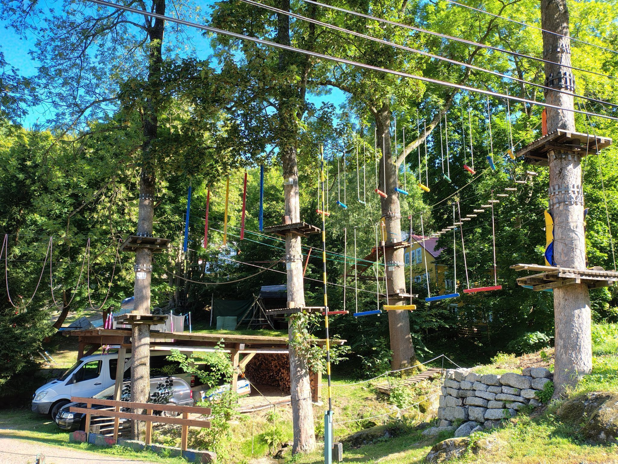 An outdoor adventure park with rope bridges, wooden platforms, and a stone wall.