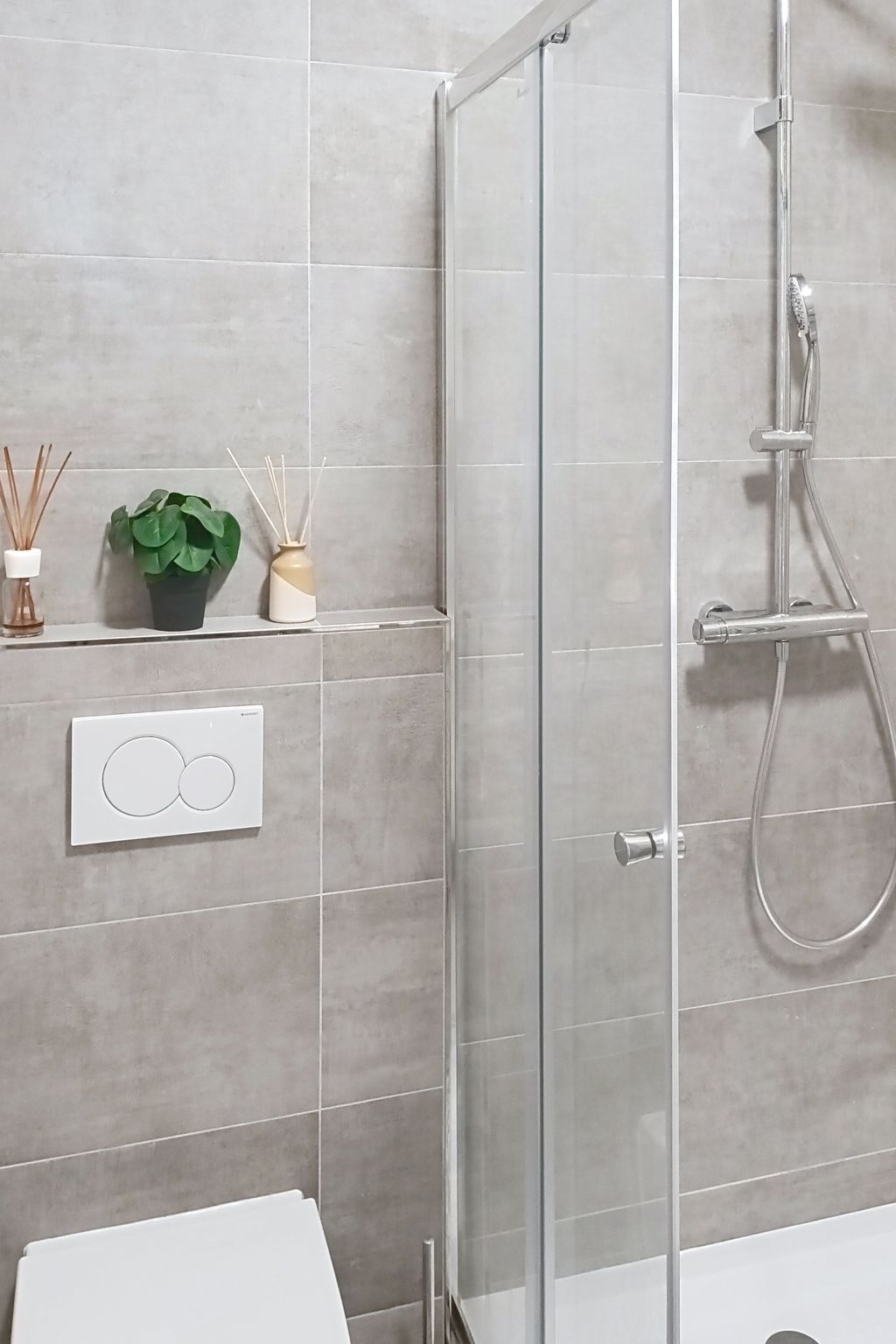 Ein modernes Badezimmer mit Duschkabine aus Glas, Toilette und Wanddiffusor mit Schilfstäbchen.