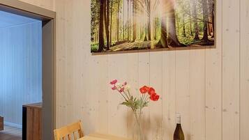 Ein Holztisch mit einem Waldbild, einer Blumenvase und einer Weinflasche.