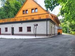 Een tweelaags houten gebouw met een schuin dak, een klein terras en een geplaveid pad.