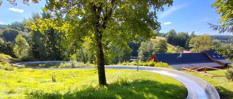 A metal slide in a grassy area with trees and a building in the background.
