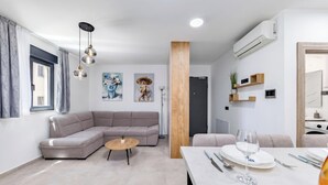 Ein modernes Wohnzimmer mit einer Eckcouch, einem runden Couchtisch und einem Essbereich mit Tisch für zwei Personen.