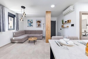 Ein modernes Wohnzimmer mit einer Eckcouch, einem runden Couchtisch und einem Essbereich mit Tisch für zwei Personen.