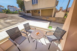 Ein Balkon mit Korbstühlen und einem Tisch, einem weißen Geländer sowie Blick auf eine Straße und Gebäude.