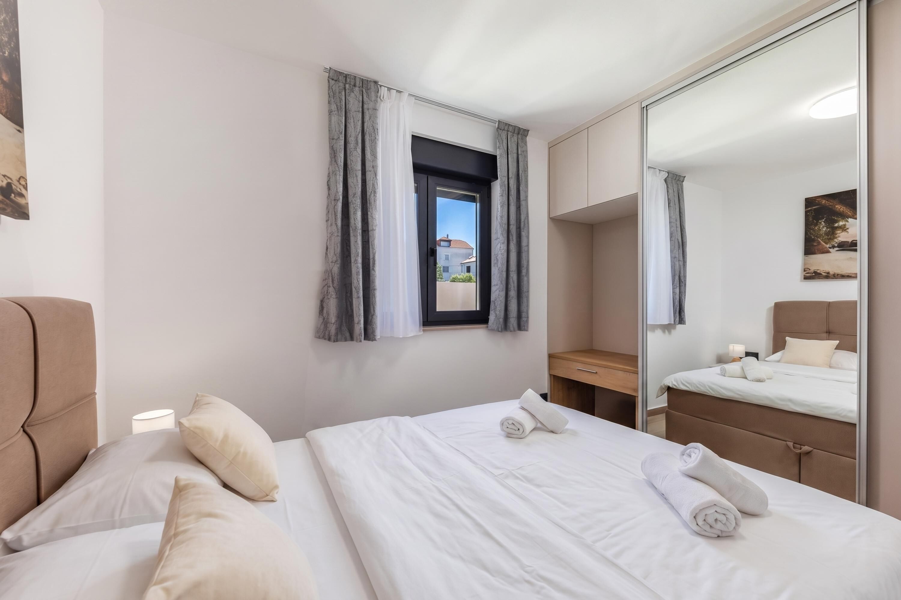 Habitación de hotel con dos camas, un espejo grande, una ventana con cortinas y vistas al exterior.