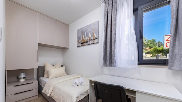Ein Schlafzimmer mit Bett, Schreibtisch, Stuhl, Nachttisch und einem Fenster mit Vorhängen.