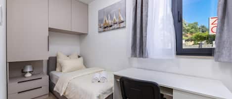 Un dormitorio con cama, escritorio, silla, mesita de noche y ventana con cortinas.