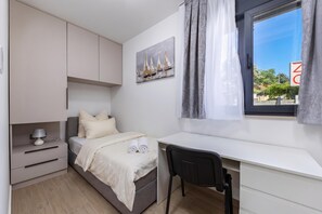 Una camera da letto con un letto, una scrivania, una sedia, un comodino e una finestra con tende.
