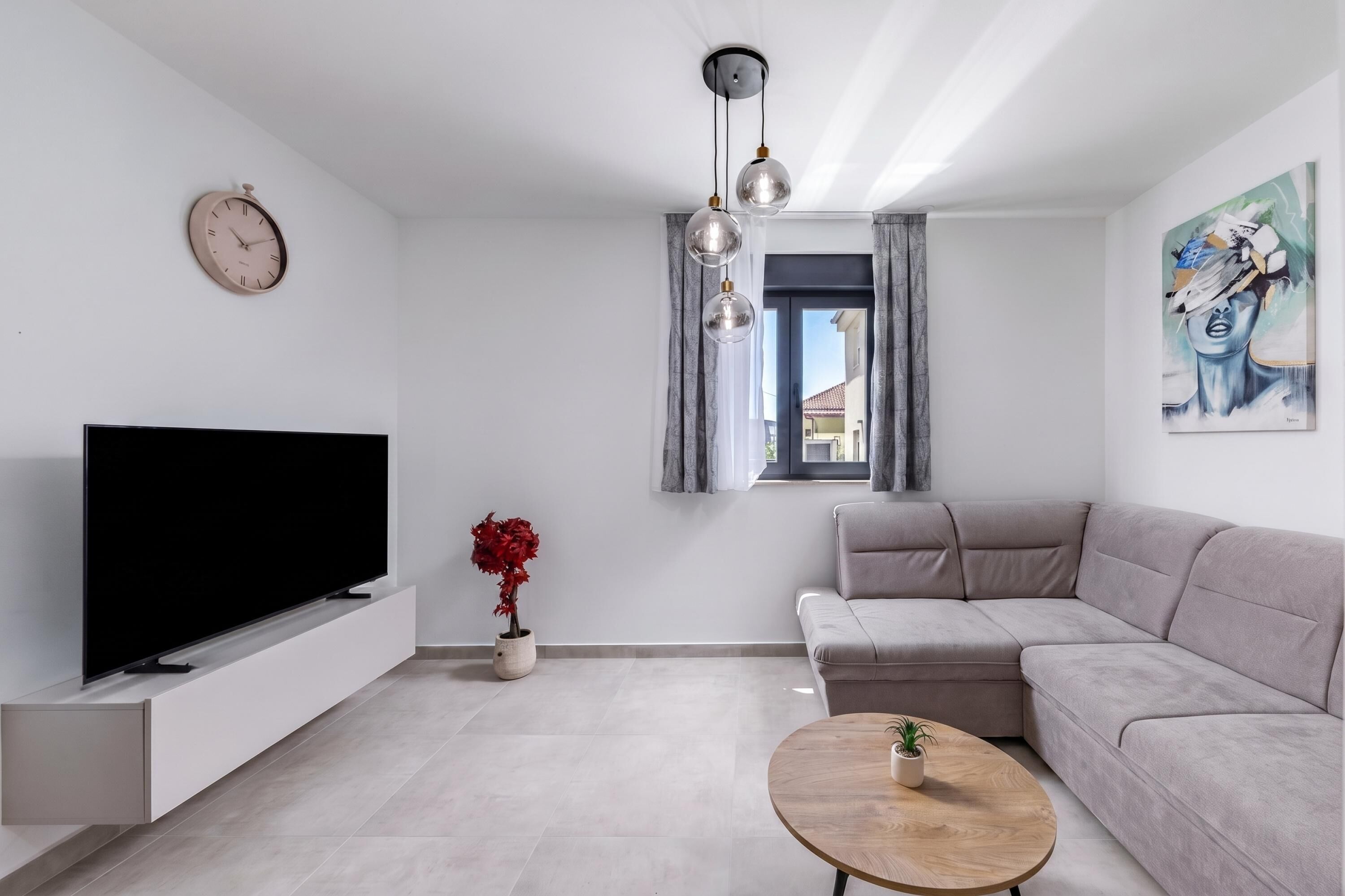 Ein modernes Wohnzimmer mit Flachbildfernseher, einer Couch, einem Couchtisch, einer Zimmerpflanze und einem Bild an der Wand.