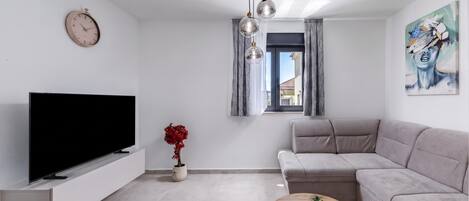 Ein modernes Wohnzimmer mit Flachbildfernseher, einer Couch, einem Couchtisch, einer Zimmerpflanze und einem Bild an der Wand.
