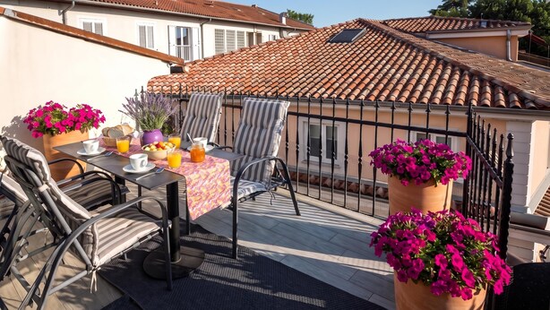 Terraço com mesa posta para o café da manhã, área de estar externa e vasos de flores.