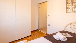 Quarto de hotel com cama, piso de madeira, guarda-roupa branco e porta que dá para outro cômodo.