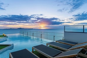 A poolside area with lounge chairs and a glass railing overlooking the sea during sunset. - Sea View Large Luxury Space Beach Front (Pattaya)