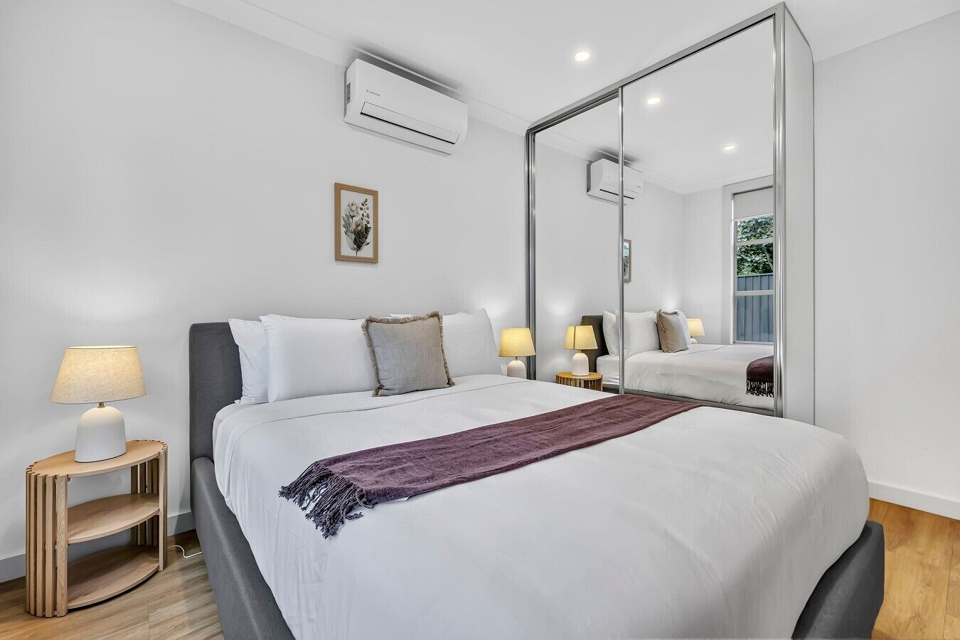 A hotel room with a large bed, two bedside tables with lamps, a mirror, and an air conditioning unit.