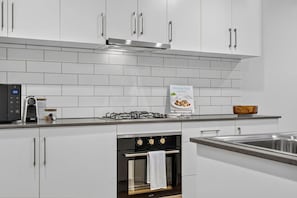 A modern kitchen with white cabinetry, a gas stove, a built-in oven, and a digital clock.