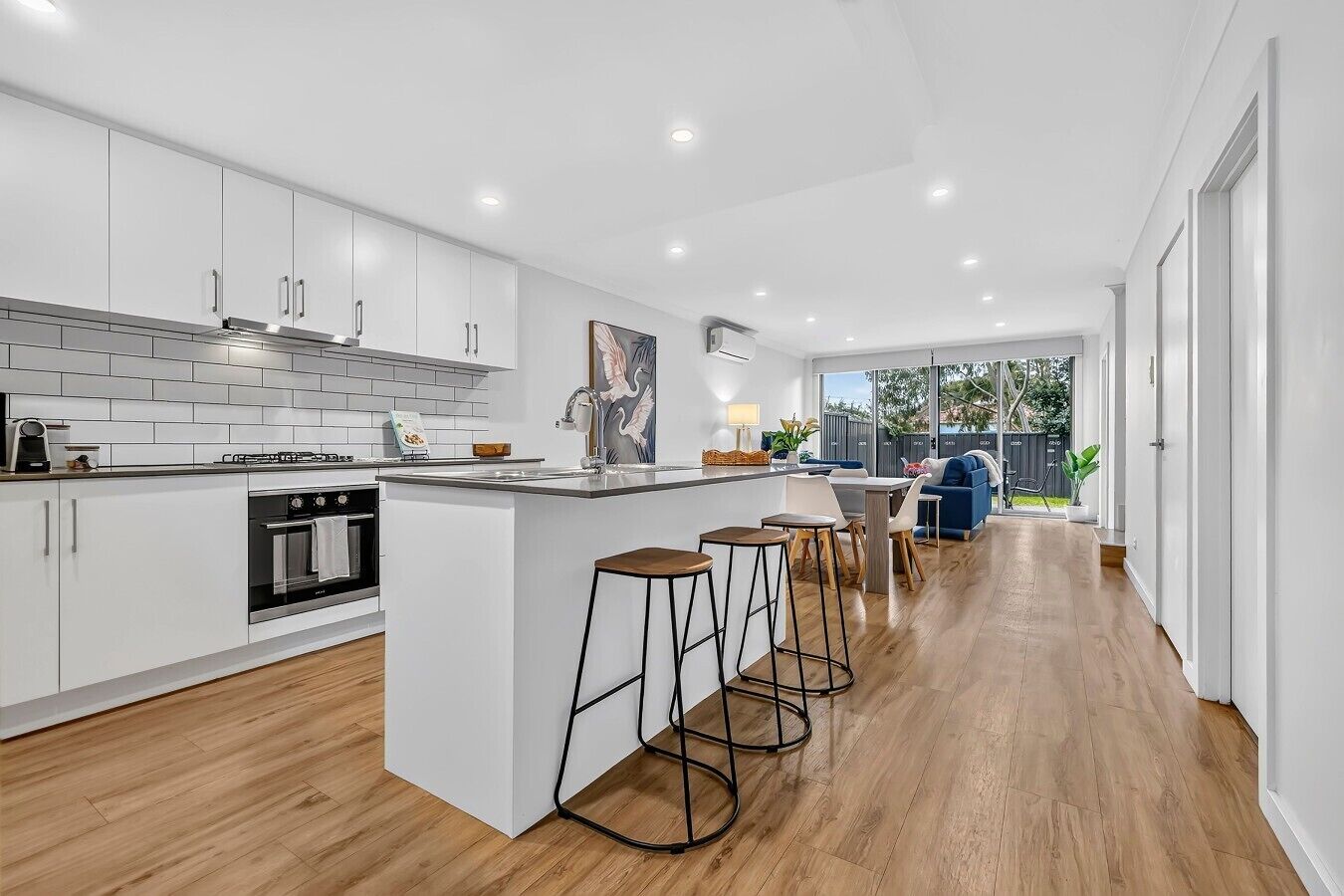 A modern kitchen with white cabinetry, a built-in oven, and a central island with bar stools.