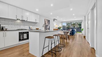 A modern kitchen with white cabinetry, a built-in oven, and a central island with bar stools.