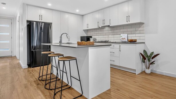A modern kitchen with white cabinetry, a black refrigerator, a gas stove, and a bar stool area.