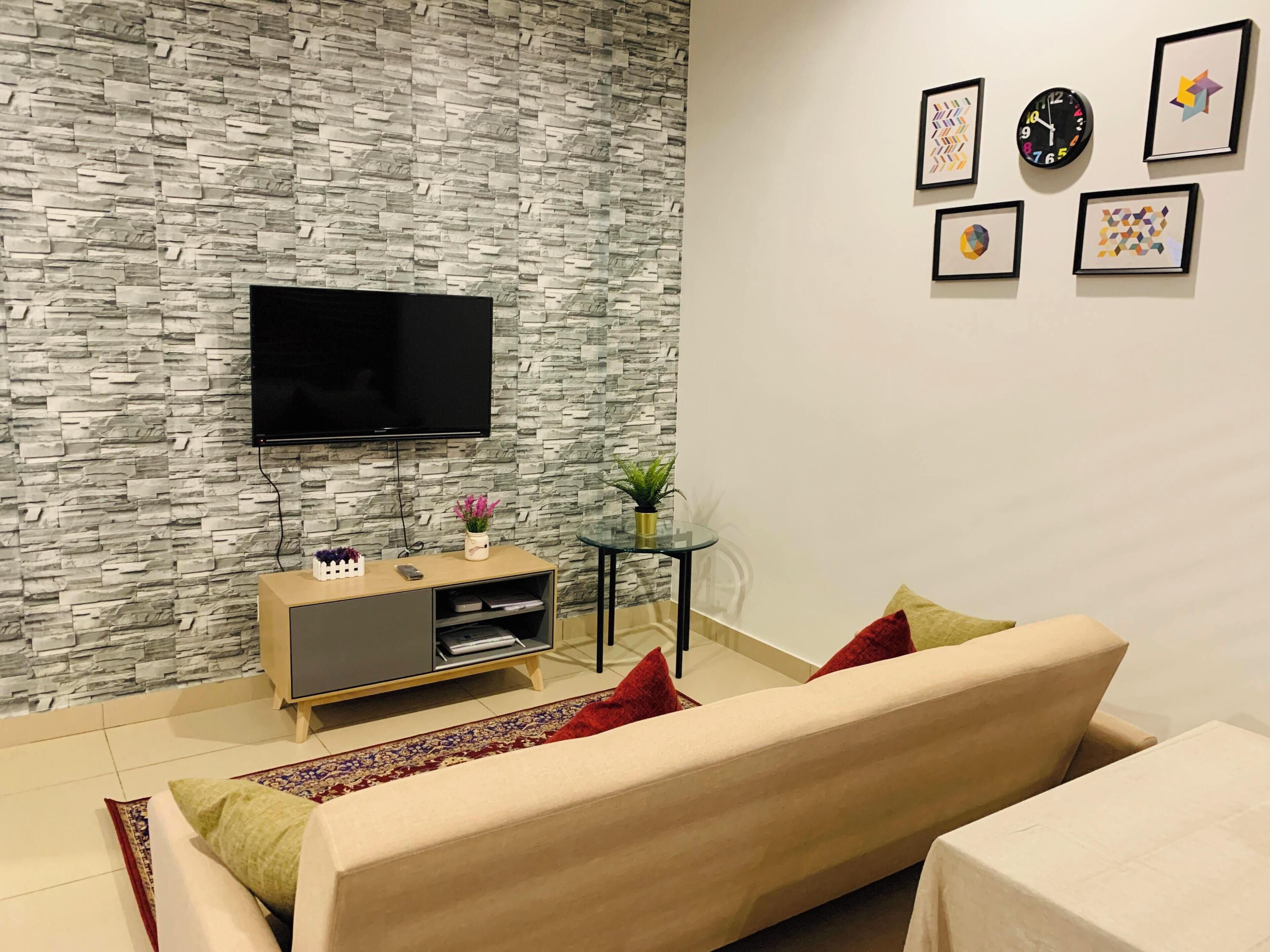 Un salon avec un mur en pierre, un téléviseur à écran plat, un canapé, une table basse et une petite table d’appoint avec une plante.
