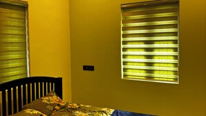 A room with a bed, a window with blinds, a ceiling fan, and a wall-mounted air conditioning unit. - Tranquil 2-bedroom house with AC in delightful Varkala (Varkala)